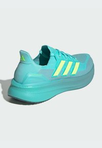 Teal running shoe with mesh upper, bright yellow accents, structured heel, and a thick textured sole featuring the "Ultraboost" label.