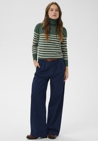 Zelena prugasta dolčevita u kombinaciji sa širokim, rastezljivim farmerkama u tamnoplavoj barvi. Rjava pasica i črne čevlje dopolnjujejo videz.