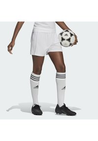 Shorts de football blancs et crampons noirs, accompagnés de chaussettes blanches montant jusqu'aux genoux ornées de trois rayures noires, tenant un ballon de football en noir et blanc.
