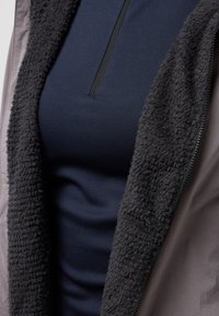 Navy blue long-sleeve top with a textured black fleece lining, partially unzipped, framed by a grey outer layer. Textured fabric and zippers visible.