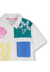 Κοντομάνικο πουκάμισο από λευκό ύφασμα με πολύχρωμα σχέδια: ροζ κοχύλι, πράσινο αστερίες, κίτρινες κυματιστές γραμμές και μπλε τσέπη. Κούμπωμα με κουμπιά.