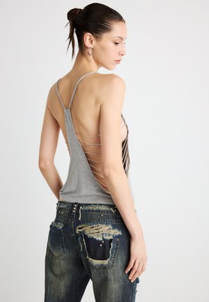 Hall halli tank top sügava U-kaelusega seljal, ristkäistega; kombineeritud kulunud tume teksapükstega, millel on karvased detailid.