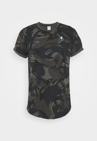 Camiseta de manga corta en patrón de camuflaje oscuro, hecha de algodón. Presenta un cuello redondo y un dobladillo ligeramente curvado. Logo distintivo en el pecho.