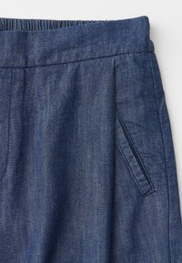 Pantalon à taille élastique bleue doté de poches latérales inclinées et de coutures visibles sur un tissu à texture denim.