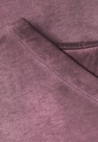 Bomuldsstof i dæmpet mauve farve, med v-hals design og fin ribbet tekstur, samt synlige sømdetaljer.