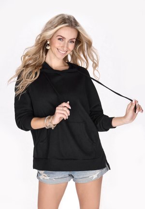 Zwarte hoodie met een gestructureerd oppervlak, voorzak en verstelbare koord, gecombineerd met verwassen denim shorts.