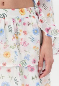 Robe florale blanche avec un design à volants comprenant diverses fleurs multicolores et des papillons. Tissu doux et transparent avec des manches volantes.