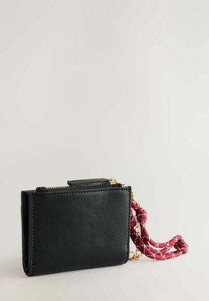 Must kullane nahkrahakott, millel on kuldne tõmblukk ja millel on punane ja valge punutud kammide külge seotud aksessuaar. Sujuv tekstuur ja kompaktne ristkülikukujuline kuju.