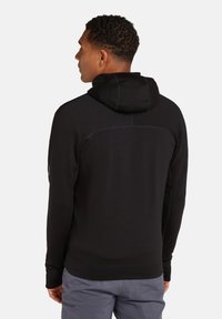 Zwarte hoodie met een ontspannen pasvorm, voorzien van een zachte textuur, contrasterende stiksels en een buidelzak.