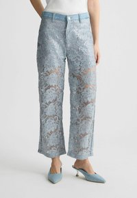 Pantaloni azzurri con paillettes che presentano un motivo di pizzo floreale, design a gamba larga e vita in denim. Abbinati a tacchi blu con decorazioni.