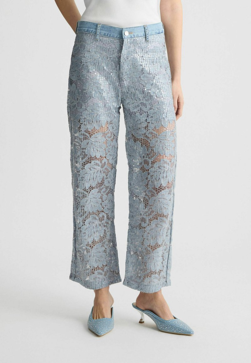 Pantaloni azzurri con paillettes che presentano un motivo di pizzo floreale, design a gamba larga e vita in denim. Abbinati a tacchi blu con decorazioni.