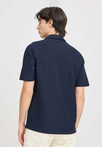 Mørkeblå kortærmet polo-shirt i tekstureret materiale, med krave og lige kant. Enkel og alsidig design.