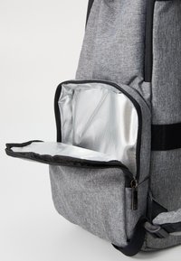 Γκρι σακίδιο υφάσματος με τσέπη μπροστά με φερμουάρ. Η τσέπη έχει εσωτερικό ασημί, μονωμένο, και μαύρες λουρίδες για στήριξη.