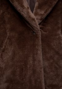 Manteau en fausse fourrure marron foncé avec de larges revers et un seul bouton noir visible sur la fermeture frontale.
