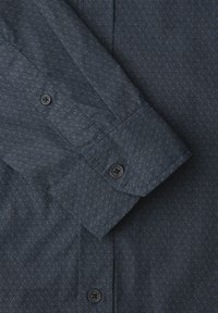 Chemise à manches longues gris foncé avec motif géométrique de cubes, poignet boutonné et boutons noirs avec texte autour du bord.