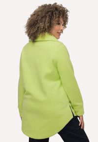 Limettengrüne Fleecejacke mit Kragen, geschwungenem Saum und seitlichen Schlitzen. Verfügt über lange Ärmel und eine weiche, strukturierte Oberfläche.