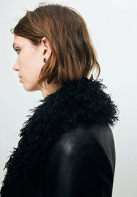 Jachetă din piele neagră cu un guler din blană neagră texturată și pufoasă. Stilizată cu o coafură castanie de lungime medie, văzută din lateral.