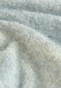 Šviesiai pilkas tekstūruotas audinys su minkštu, pūkuotu paviršiumi; turi mažų kilpelių ir skaidulų raštą, sukuriantį jaukų įvaizdį.