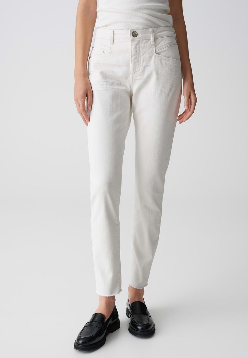Jeans in denim bianco con una vestibilità slim, gamba dritta, vita media e orlo grezzo. Abbinati a mocassini neri per un contrasto.