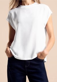 Top bianco a maniche corte con scollatura a girocollo, caratterizzato da una vestibilità rilassata e una texture liscia. Abbinato a jeans blu scuro.