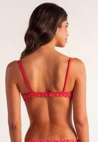 Top de bikini rojo con tirantes finos, que presenta un patrón texturizado. Cierre trasero ajustable y un diseño liso y ajustado.