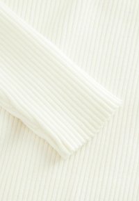 Tissu blanc côtelé avec une texture douce, comportant des lignes horizontales et un bord légèrement effiloché d'un côté. Convient à la confection de vêtements.