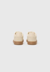 Beige suede sneakers with a rubber gum sole, rounded toe, and smooth stitching details. Designed for casual wear with a low-top silhouette.