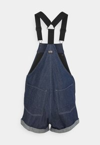 Salopette courte en jean bleu foncé avec bretelles noires ajustables et deux grandes poches avant, avec une petite étiquette G-Star sur le panneau poitrine.