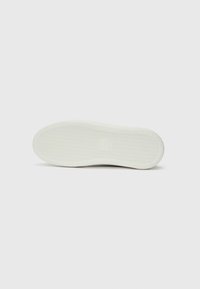 Bodem van een sneaker met een gestructureerd rubberen oppervlak, voornamelijk wit, met een cirkelpatroon langs de randen en een vlak ontwerp.