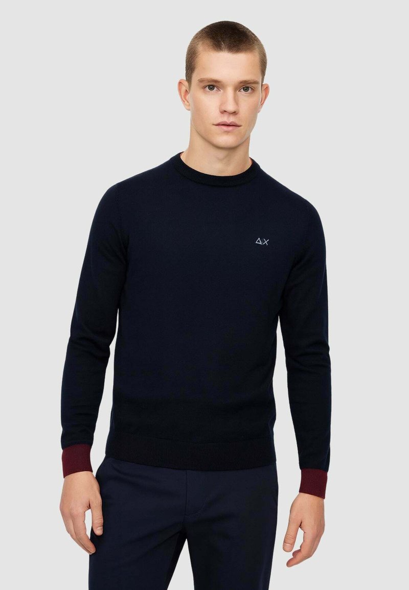 Maglione azzurro navy in maglia con scollo rotondo, polsini a coste color bordeaux e piccolo logo sul petto. Texture liscia e design aderente.