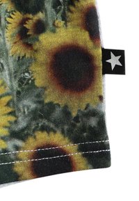 Hihna kankaan vaatteessa, jossa on auringonkukka-kuvio, joka sisältää keltaisia terälehtiä ja tummia keskikohtia. Mukana musta etiketti, jossa on valkoinen tähkäkuvio.