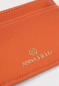Porte-cartes en cuir orange avec logo Anna Field doré et plusieurs emplacements pour cartes, présenté en gros plan.