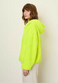 Fuzzy neon green oversized hoodie with a drawstring hood and front pocket, featuring a soft texture and relaxed fit.