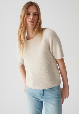 Pull à manches courtes couleur crème avec une finition douce et texturée. Associé à un jean en denim bleu clair, avec une coupe décontractée.