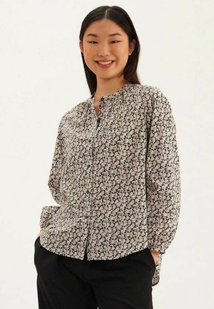 Chemise à boutons florale en noir et blanc, arborant des manches longues, un col mandarin, et une coupe décontractée avec un motif de petites fleurs sur toute la surface.
