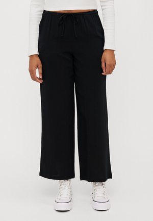Schwarze weite Hosen mit elastischem Bund und verstellbarem Kordelzug. Glattes, leichtes Material, ergänzt durch weiße High-Top-Schuhe.