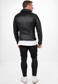 Zwarte leren jack met een gestikte textuur, hoge kraag, ritszakken en een aansluitende vorm. Gemaakt boven een zwarte spijkerbroek en witte sneakers.