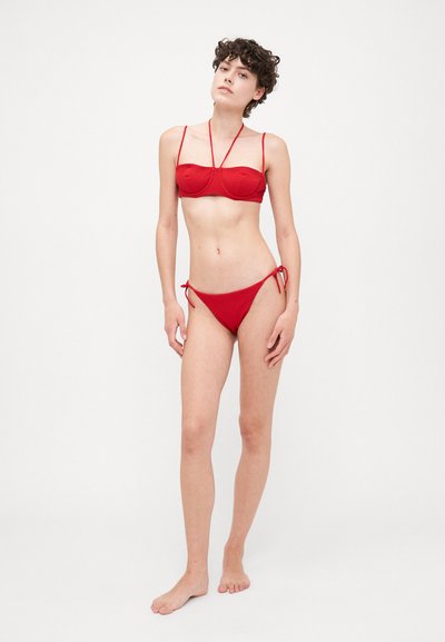 Sarkans bikini komplekts ar bandeau topu ar plānajām siksniņām un teksturētu audumu, kopā ar zemu jostasvietu apakšdaļām, kas sasaistās sānos.