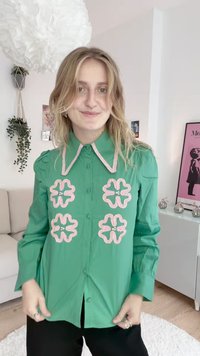 Zelena srajca s kratkimi rokavi, okrašena s rožnatim vezenim cvetličnim vzorcem spredaj in napihnjenimi rokavi, z ostro ovratnico in gladko teksturo.