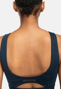 Donkerblauw sporttop met een scoop rugontwerp, voorzien van brede banden en een uitsnijding. Glad materiaal met een subtiele glans.