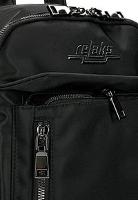 Zaino nero realizzato in tessuto resistente; presenta tasche con zip, design elegante e logo stampato in rilievo; include accessori in argento lucido.