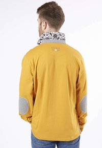 Chemise jaune avec un col à motifs, des coudières grises et des détails de boutons sur les manches. Offre une coupe décontractée et une texture douce.