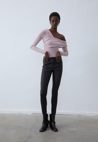 Hosszú ujjú, váll nélküli rózsaszín bodysuit, ráncolt részletekkel, vékony szabású fekete nadrággal és fekete bokacsizmával párosítva. Simaságot biztosító anyag, testhezálló dizájn.