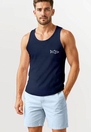 Navy tank top with an embroidered white shark design on the left side; worn with light blue shorts; smooth fabric; casual fit.