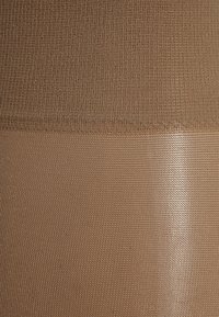 Collant beige senza cuciture con una texture liscia, caratterizzati da una fascia in rilievo a contrasto. Il tessuto appare morbido e flessibile, con cuciture uniformi.