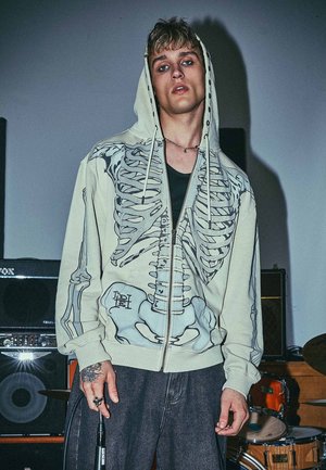 Light green hoodie with a skeleton graphic print, featuring a zip closure and drawstring hood. The design includes detailed rib and pelvic bones.
