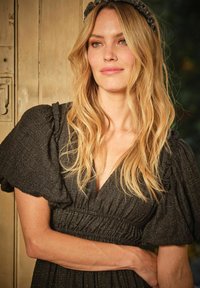 Schwarzes, strukturiertes Kleid mit Puffärmel und tiefem V-Ausschnitt. Der Stoff hat einen subtilen Glanz, und die Taille ist gerafft für eine taillierte Silhouette.