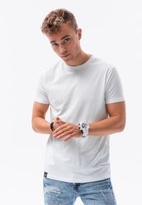 Vit bomull t-shirt med rund hals, korta ärmar och rak passform, i kombination med slitna blå jeans. Svart och vita handledsaccessoarer.