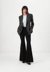 Sacou negru cu dungi subțiri peste un top ribbed de culoare albastru deschis, asortat cu pantaloni negri evazați și pantofi negri. Material fin și croială ajustată.