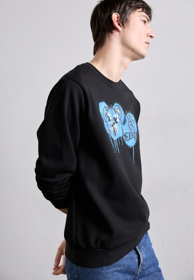 Sweatshirt noir avec un graphique bleu représentant un ours et un motif de main. Il dispose de poignets et d'un ourlet côtelés, fabriqué dans un tissu doux et résistant.